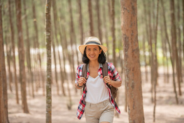 people and lifestyles adventure, travel, tourism, hike and people concept - traveller women walking in the forest of smiling  walking with backpack, hat in woods.