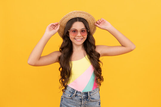 happy kid in summer straw hat and glasses has curly hair on yellow background, summer vacation