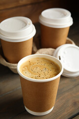 Takeaway paper coffee cups with plastic lids and cardboard holder on wooden table