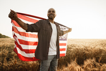 African american young man holding USA national flag through wheat field