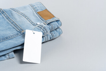 Jeans clothing white paper tag, label blank mockup template, to place your design. On a blue jeans and grey background, copy space, flat lay