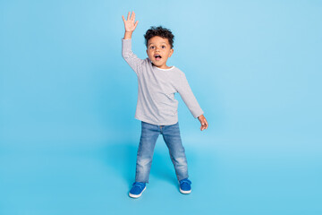 Full length body size view of attractive friendly cheerful boy waving hi isolated over bright blue...