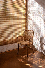 Rattan wicker chair with sunlight shining through wooden blinds