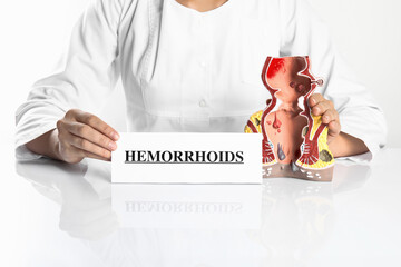 Doctor holding card with word Hemorrhoids and model of unhealthy lower rectum on white background,...