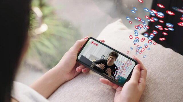 Close up woman watching smartphone at home. Asian man musician vlogger streaming live broadcast video on screen mobile with a lot of emoji like and emotion love. People watching video live streamings