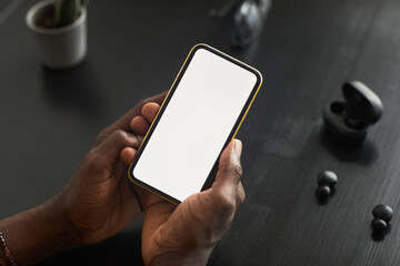 Close-up of man holding mobile phone with empty touch screen in his hands and using new application at the table