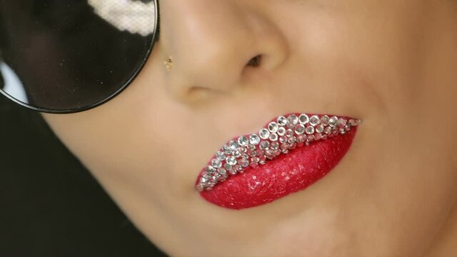 Closeup of a beautiful woman lips with beautiful diamond, red make up and sunglasses sending air kiss . Close up of girl's mouth having flirty emotions and sending air kiss .	
