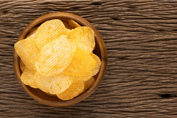 tasty ridged potato chips in wooden bowl on rustic natural wood texture background with copy space for text, harmony brown tone, top view