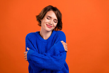 Photo of nice brunette hair millennial lady hug herself wear blue sweater isolated on orange color background