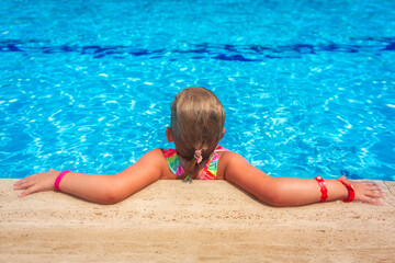 Cute little girl is relaxing in the crystal water of the pool on summer holidays.