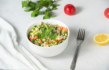 Oriental salad Tabouleh of boiled bulgur, served in a white plate, next to tomatoes, a slice of lemon and mint. On white background.