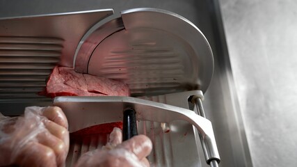 Modern semi-automatic electric frozen meat cutting machine for food processing on the table. Hands cut bacon in a slicing machine. Cutting meat on the machine.