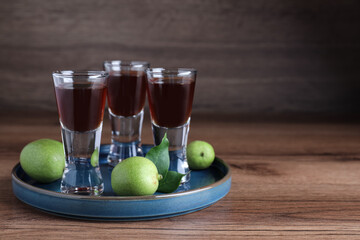 Delicious liqueur and green walnuts on wooden table. Space for text
