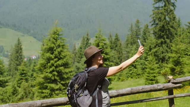 Hiking in the mountains of the USA. Young woman tourist in a beautiful hat makes a selfie in the alpine mountain. New photos on social networks.