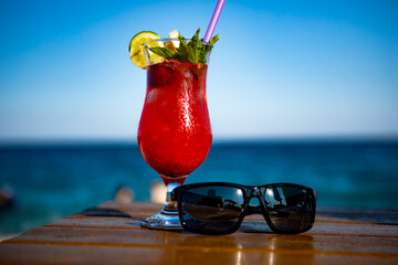 red cocktail with sunglasses on the seashore on a wooden table