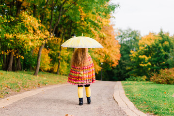 Happy child girl laughing with an umbrella in the autumn park