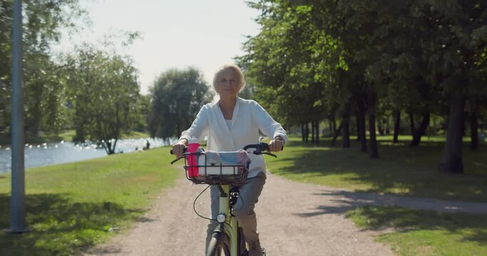 Slider shot of old woman riding bicycle in summer park