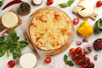 Delicious khachapuri with cheese surrounded by different products on white wooden table, flat lay