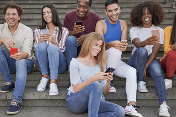Obraz premium Group of young diverse friends using mobile phone in the city - Multiracial people having social moment and enjoy technology