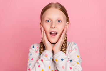Photo of excited charming school girl wear dotted pullover arms cheeks open mouth isolated pink...