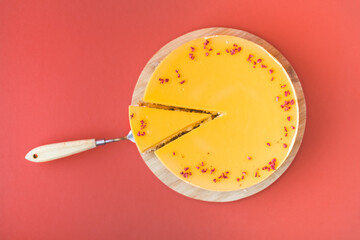 Cheesecake cut with yellow mango mash layer on the red background