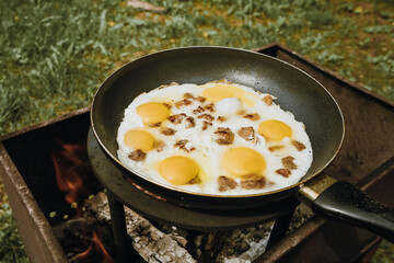 Frying pan of fried eggs and bacon, green grass on the background, cooked on the grill on a summer sunny day, summer breakfast, eating in nature - the concept of a healthy lifestyle