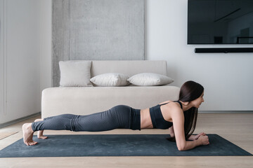 Slim woman standing in plank during training at home