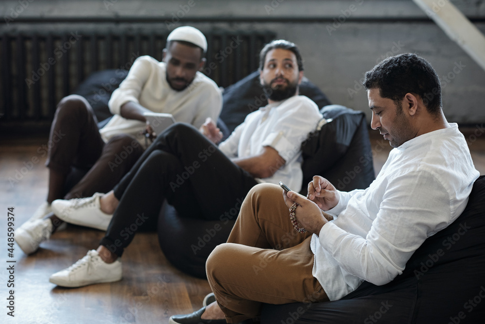 Aufkleber mixed-race manager scrolling in smartphone while sitting in armchair against colleagues