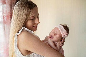 Portrait of young Caucasian mother holds hug little newborn baby two weeks old at home. Happy mom embraces small infant child, shows love and care, childcare concept