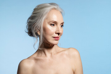 Senior female with flawless skin and bare shoulders, portrait on blue with copy space. Gray haired...