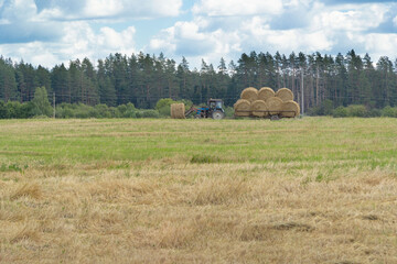 Fototapeta premium tractor with rolls of straw at the far end of the field. In the distance forest