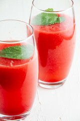 Top view of two glasses of watermelon juice with mint leaf, selective focus, on table and white background, in vertical