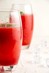 Close-up of two glasses of watermelon juice with mint leaf, ice, selective focus, on table and white background, vertical