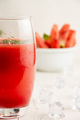 Close-up of glass of watermelon juice with mint leaf and bowl with watermelon, selective focus, on table and white background, vertical