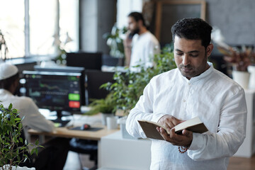 Contemporary mixed-race businessman reading book in large open space office