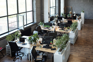 Group of desks with computer monitors standing along large windows in office or classroom