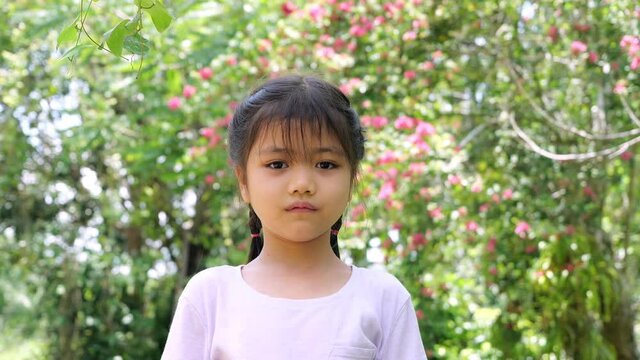 slow motion video of Adorable asian children girl Braids and broken tooth, funny faces are smiling and laughing , bright and cute in the garden.
