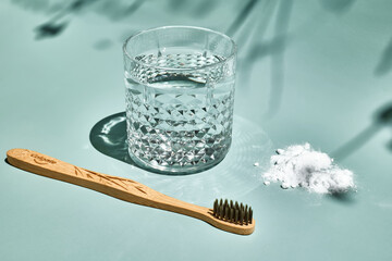 Bamboo toothbrush and glass of water on light green pastel background with shadows of natural light. Plastic free, zero waste, eco cosmetics and sustainable lifestyle concept