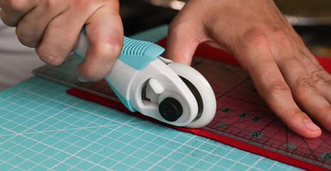 Designer cutting red fabrics with roller knife on rubber board