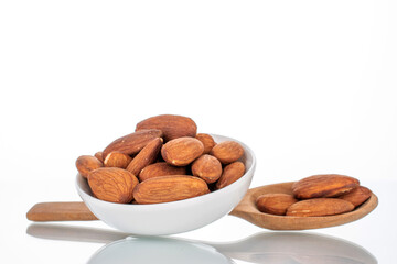 Fragrant roasted almonds in a white ceramic bowl with a wooden spoon, close-up, isolated on white.
