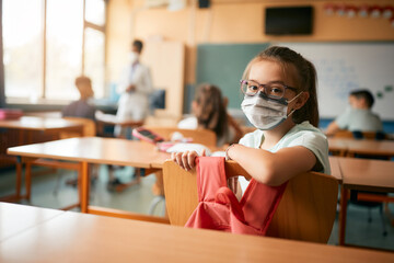 Schoolgirl wearing protective face mask in classroom and looking at camera.