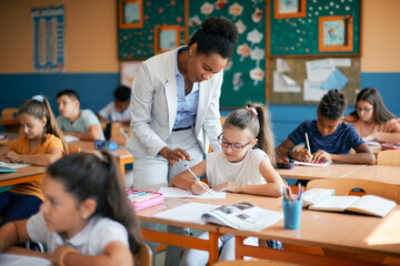 African American female teacher assisting schoolgirl during class at elementary school.