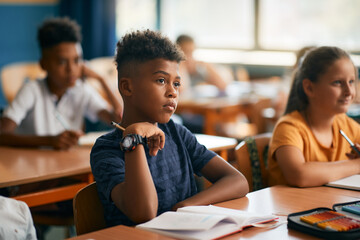 African American schoolboy and his classmates paying attention during class in classroom.