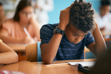 Uncertain African American schoolboy having exam during class in classroom.