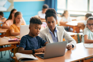 African American teacher and her student using laptop during computer class at elementary school.