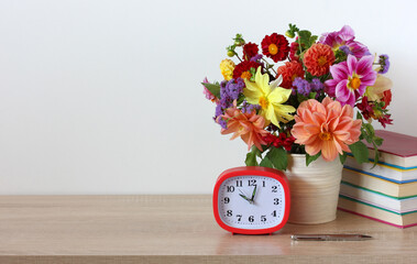 bouquet of dahlias, an alarm clock and textbooks on the table