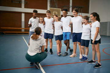 Multi-ethnic group of happy kids having fun with their PE teacher at school gym.