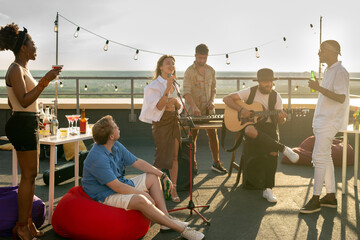 Music group performing for intercultural friends at rooftop party