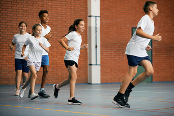 Group of elementary students running while having PE class at school gym.