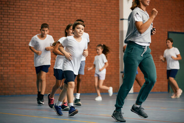 Elementary students and their PE teacher running during class at school gym.